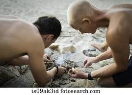 Two mid adult men lighting bonfire on beach
