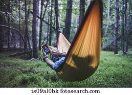 Hiker lying in hammock in forest using digital device