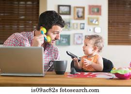 Man and baby sitting at kitchen counter playing with smartphone and toy phone