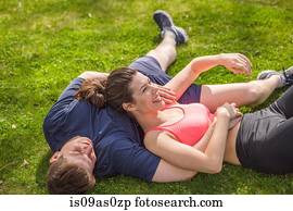 Romantic young sporty couple lying on park grass