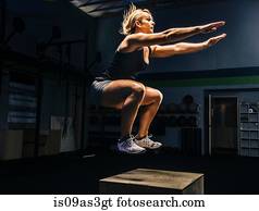 Young woman jumping mid air on gym box with arms reaching out