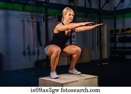 Young woman squatting on gym box with arms reaching out