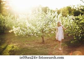 Full length front view of young woman wearing sleeveless dress standing in orchard looking away smiling