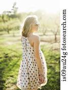 Rear view of young woman in orchard wearing sleeveless dress and sunglasses looking away