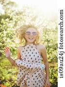 Young woman wearing sleeveless dress and sunglasses jumping looking at camera smiling