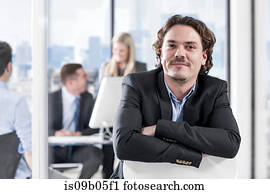 Businessman in office, colleagues chatting in background