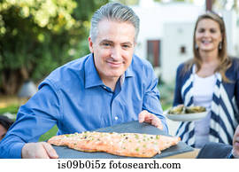 Mature man holding chopping board with fish cuisine at garden party