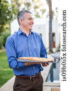 Mature man holding fish cuisine on cutting board at garden party