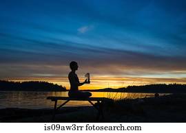 Woman practising yoga by lake at sunset