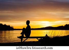 Woman practising yoga by lake at sunset