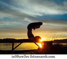 Woman practising yoga by lake at sunset