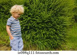 A boy walking past a bush