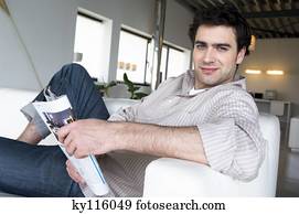 homem, mentindo, ligado, um, sofá, segurando, revista, olhando câmera