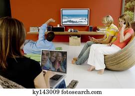 Family in living room, woman using laptop, man watching TV, 2 teens using mobile phone Family in living room, woman using laptop, man watching TV, 2 teens using mobile phone