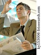 homem negócios, sentando, por, tabela, segurando jornal