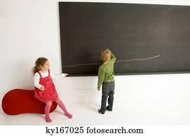 Rear view of a boy drawing on a blackboard with his sister sitting beside him