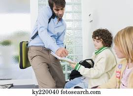 Man signing his son's notebook and talking on a mobile phone