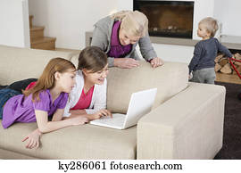 Two girls using a laptop on a couch with their grandmother standing beside them