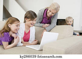 Two girls using a laptop on a couch with their grandmother standing beside them