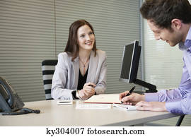 Man signing documents with a female real estate agent sitting in front of him