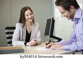 Man signing documents with a female real estate agent sitting in front of him