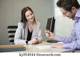 Man signing documents with a female real estate agent sitting in front of him
