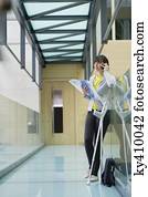 Woman holding a file and talking on a mobile phone in a corridor Woman holding a file and talking on a mobile phone in a corridor