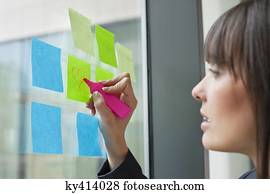 Businesswoman drawing heart shape on an adhesive note in an office Businesswoman drawing heart shape on an adhesive note in an office