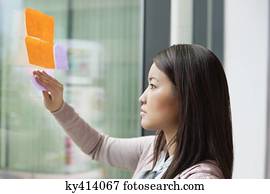 Businesswoman sticking memo notes on glass in an office