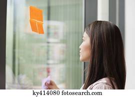Businesswoman sticking memo notes on glass in an office