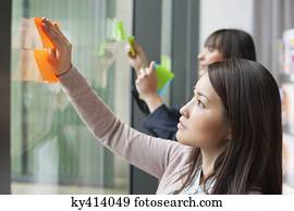 Businesswomen sticking memo notes on glass in an office