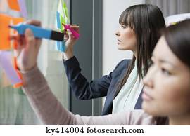 Businesswomen writing on adhesive notes in an office Businesswomen writing on adhesive notes in an office