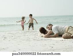 Parents lying on beach while children play in background