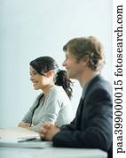 Businessman and young woman sitting at table, looking out of frame