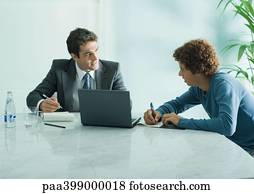 Businessman speaking to casually dressed young adult male, sitting at table