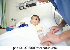 Boy lying in hospital bed holding toy car while intern checks pulse