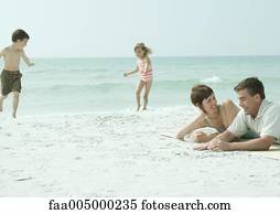 Family at the beach, parents lying on sand while children play