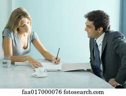 Businessman and female colleague sitting at table, woman taking notes
