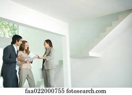 Female real estate agent showing house to young couple, pointing to blueprints