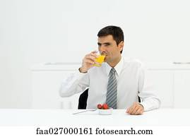 Businessman sitting at table, drinking orange juice, looking away
