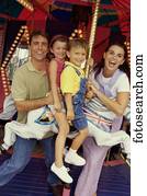 Portrait of a son and daughter sitting on a carousel horse with their parents standing beside them