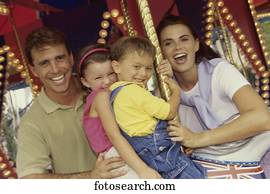 Portrait of a son and daughter sitting on a carousel horse with their parents standing beside them