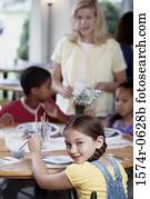 Portrait of children sitting at a table with a woman standing beside them