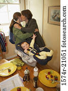 Side profile of a mid adult woman kissing her daughter with her son in a baby seat beside them