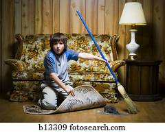 Boy sweeping dirt under rug