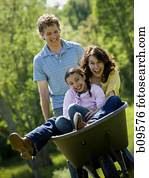 woman and her daughter sitting in a wheel barrow with a man standing beside them