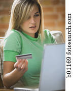 Close-up of a teenage girl holding a credit card sitting in front of a laptop