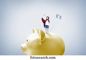 a boy with superman cape standing on top of piggy bank a boy with superman cape standing on top of piggy bank