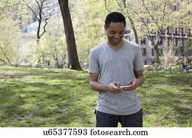 Man in casual clothing texting in park
