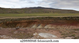 Landscape, eroded mineral rich gully through grassland, before grassy mountains